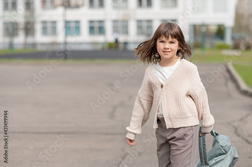 happy girl a schoolgirl of 8 years of European appearance with a backpack is walking in the school yard in the afternoon on the street looking at the camera closeup. High quality photo