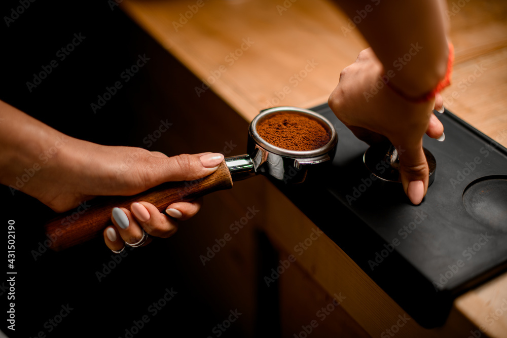 view of female baristas hand tamping coffee in portafilter before making fresh drink