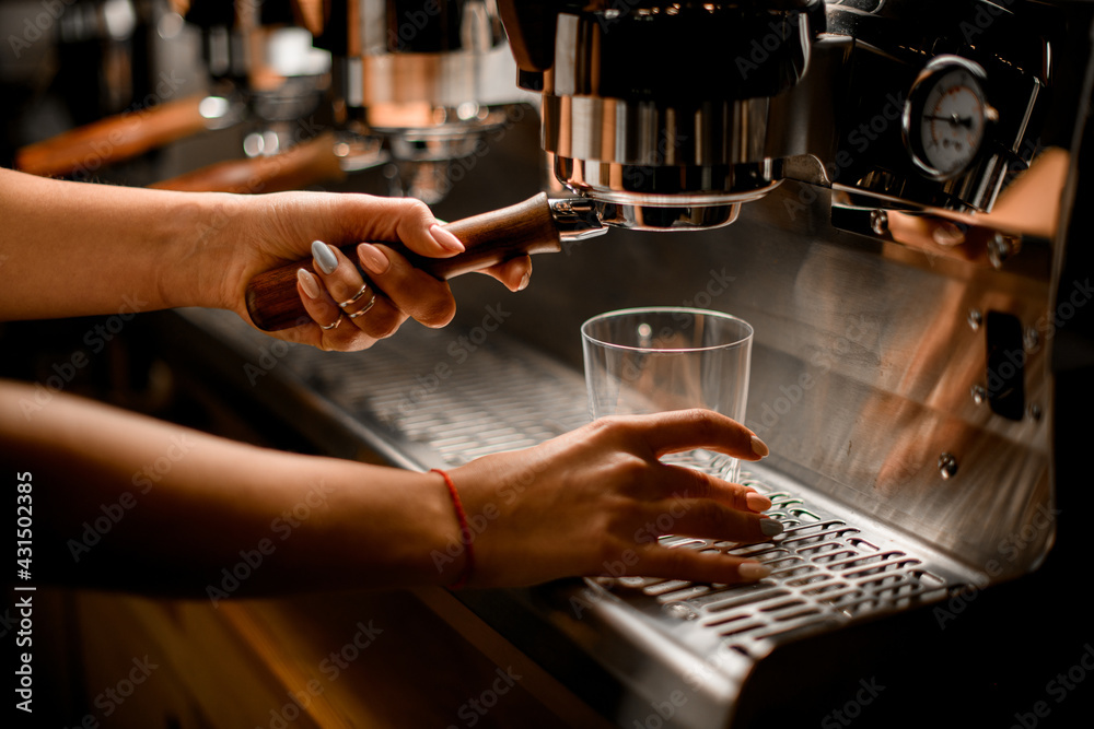 Woman barista prepares and pours coffee drink into glass with professional coffee machine