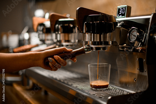 barista controls lever of modern professional coffee machine that and pours coffee drink into glass