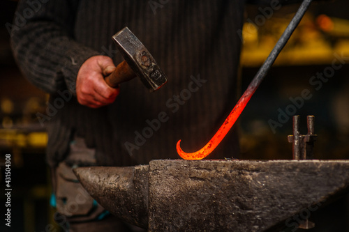 Fototapeta The blacksmith hits the red-hot workpiece in the forge with a hammer and glowing