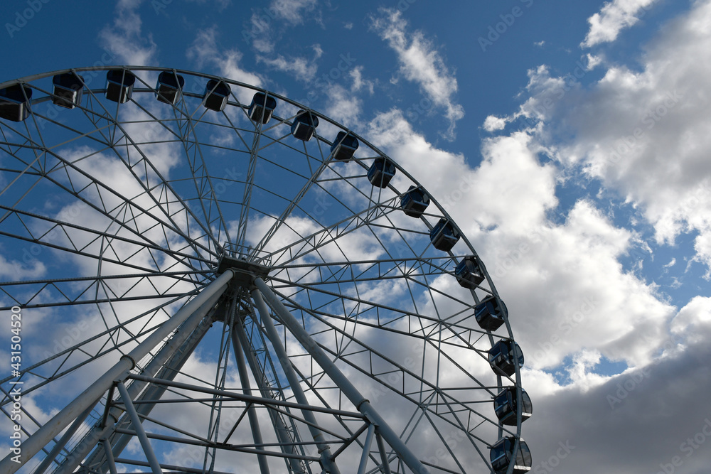 Part of the Ferris wheel with closed booths against a background of blue sky and clouds Part of the Ferris wheel with closed booths against a background of blue sky and clouds