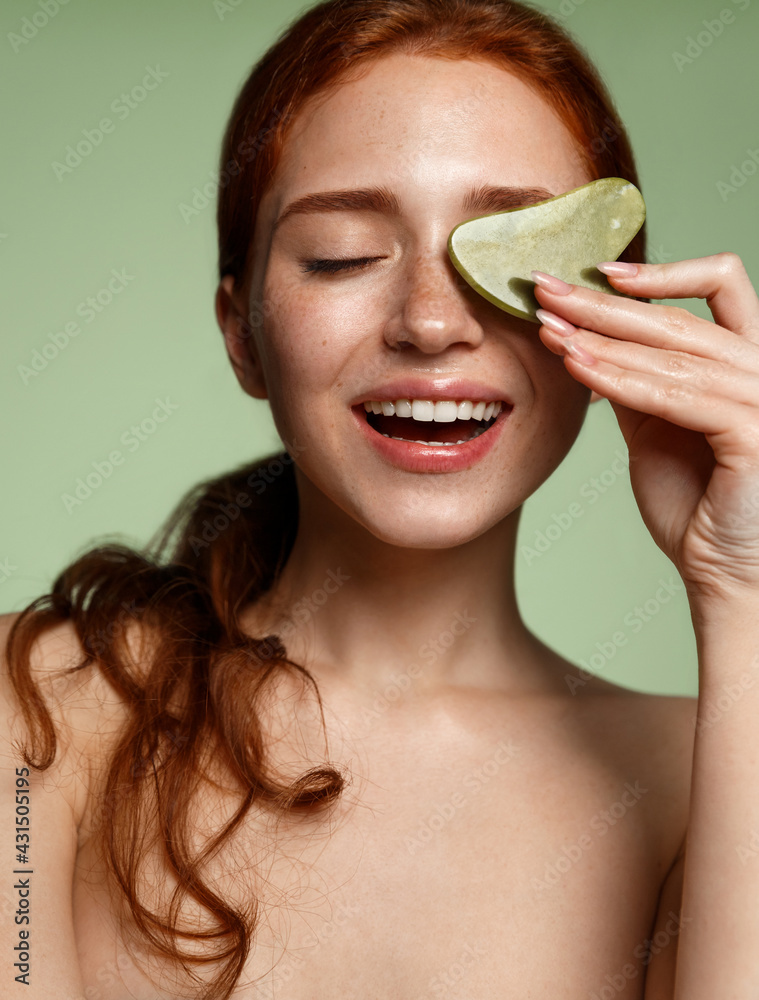 Vertical shot redhead beauty girl with glowing skin, holding natural jade gua sha scraper, smiling, tcm chinese traditional medicine on facial skin, self massage relieve muscle tension - obrazy, fototapety, plakaty 