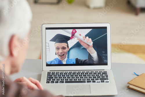 Closeup of mature man watching teenage son graduating by video chat on laptop screen