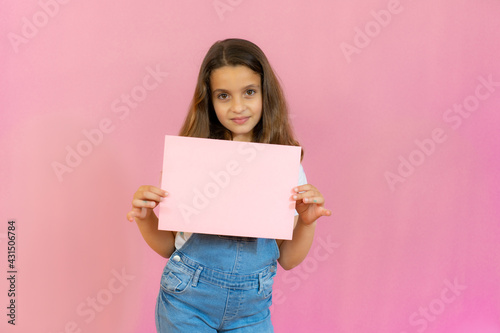 Smiling little girl holding empty pink board isolated over pink background.