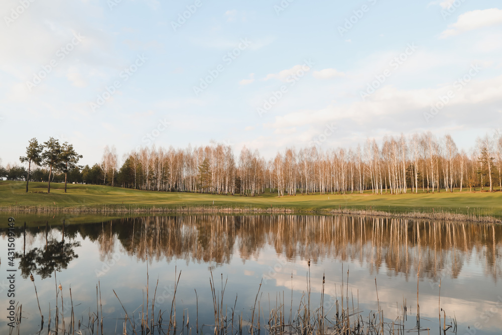 spring landscape, forest lake in spring surrounded by trees, calm water surface with reflection, bright sunlight and blue sky