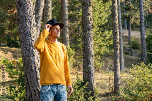 Man in black hat in the forest.Portrait caucasian tourist cowboy in yellow sweater in woodland at sunset .Beautiful landscape background with copy space.