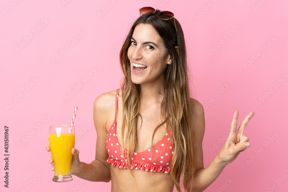 Young blonde woman over isolated pink background in swimsuit and holding a cocktail
