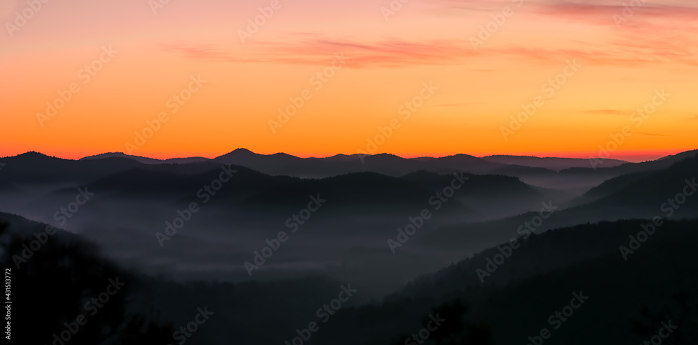 foggy, misty valley with orange sky before sunrise, beautiful orange yellow lighted sky