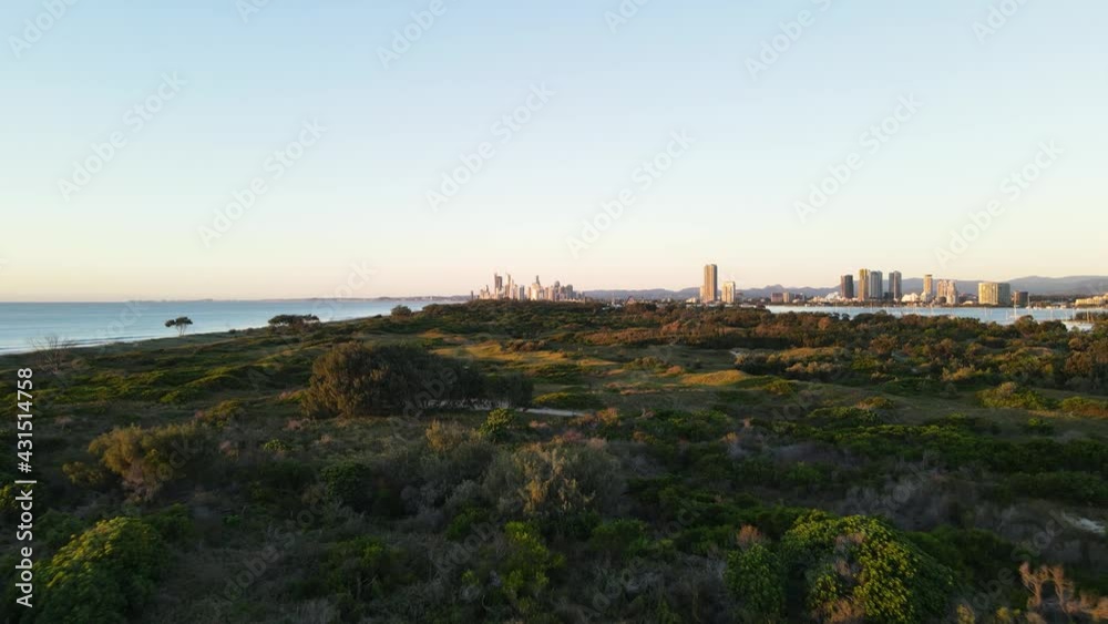 Low fast drone view travelling over a coastal nature parklands with a urban city skyline rising above in the foreground Low fast drone view travelling over a coastal nature parklands with a urban city skyline rising above in the foreground