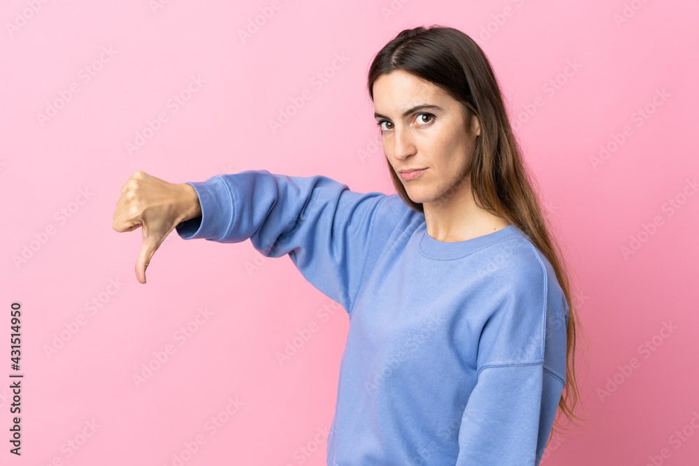 Young caucasian woman isolated on pink background showing thumb down with negative expression