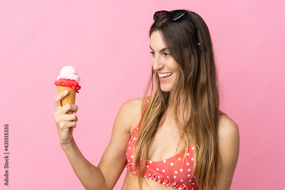Young caucasian woman holding an ice cream isolated on pink background with happy expression