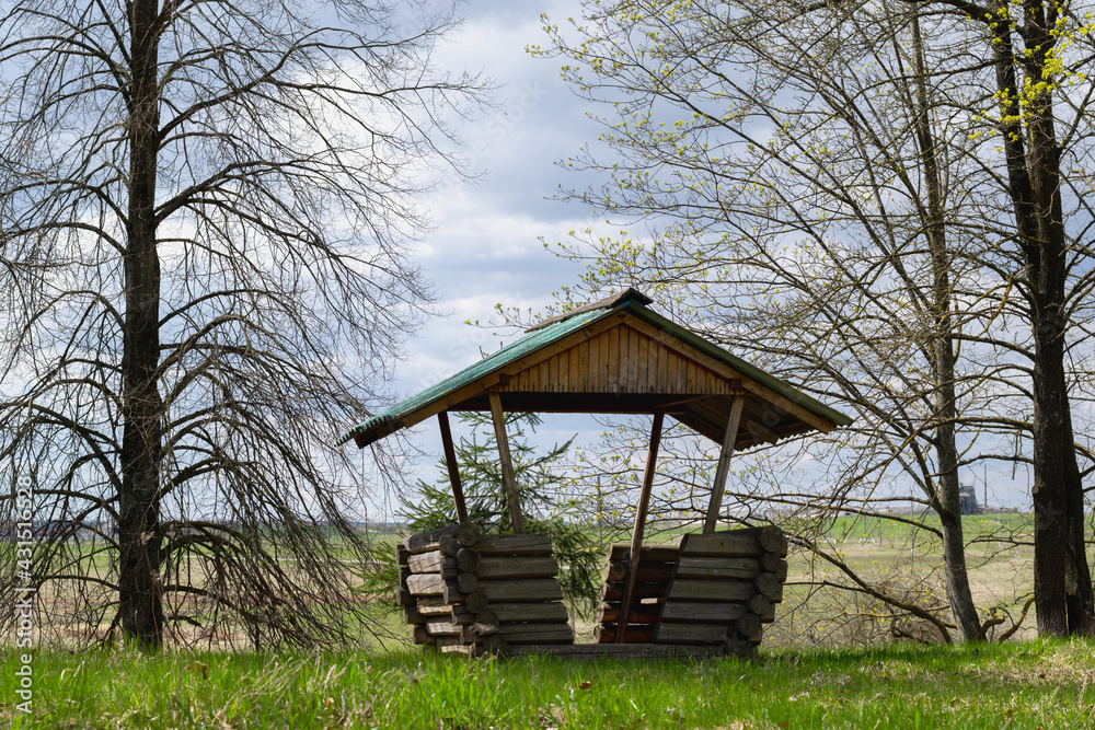 Wooden gazebo made of logs surrounded by trees outside the city against the backdrop of fields. scenery. Spring time. Horizontal photo. 
