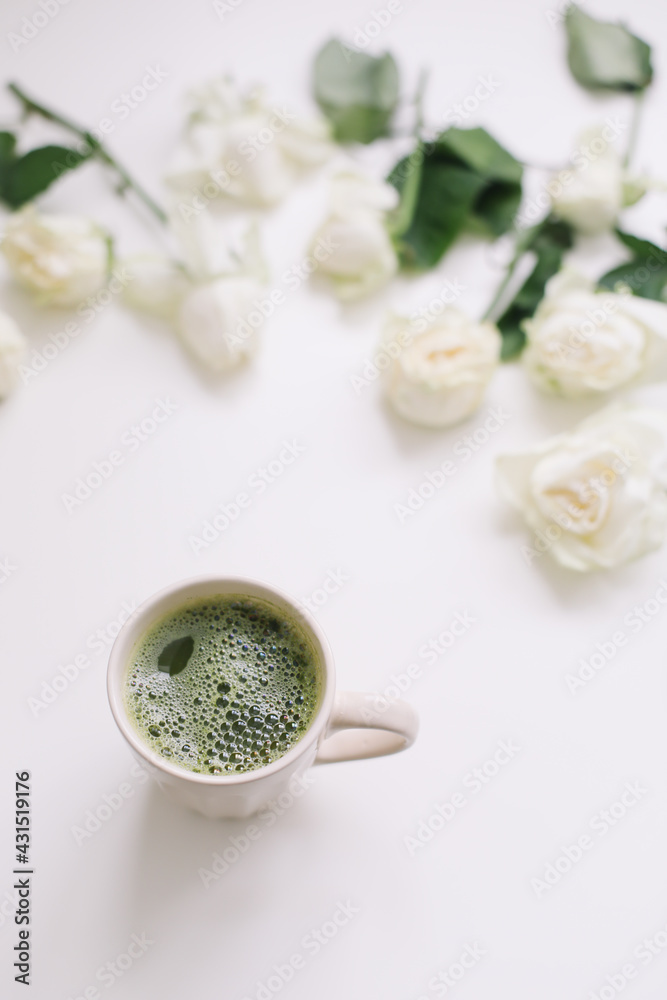 A cup of matcha tea and roses on white background. Flatlay, top view A cup of matcha tea and roses on white background. Flatlay, top view