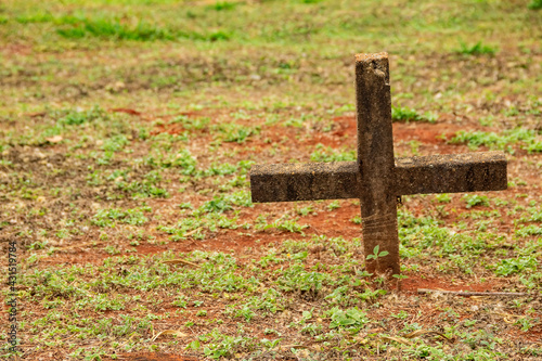 Uma cruz cravada no chão gramado sobre um túmulo.