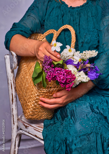 Woman holding hands wicker bag with lilac flowers indoor, Sitting on a vintage chair photo