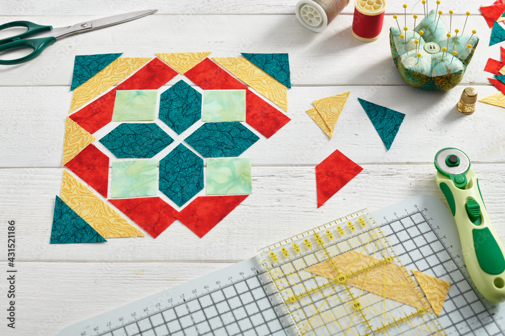 Pieces of fabric laid out in the shape of a patchwork block, sewing and quilting accessories.
