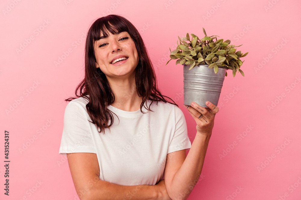 Young caucasian woman holding a plant isolated on pink background laughing and having fun. Young caucasian woman holding a plant isolated on pink background laughing and having fun.
