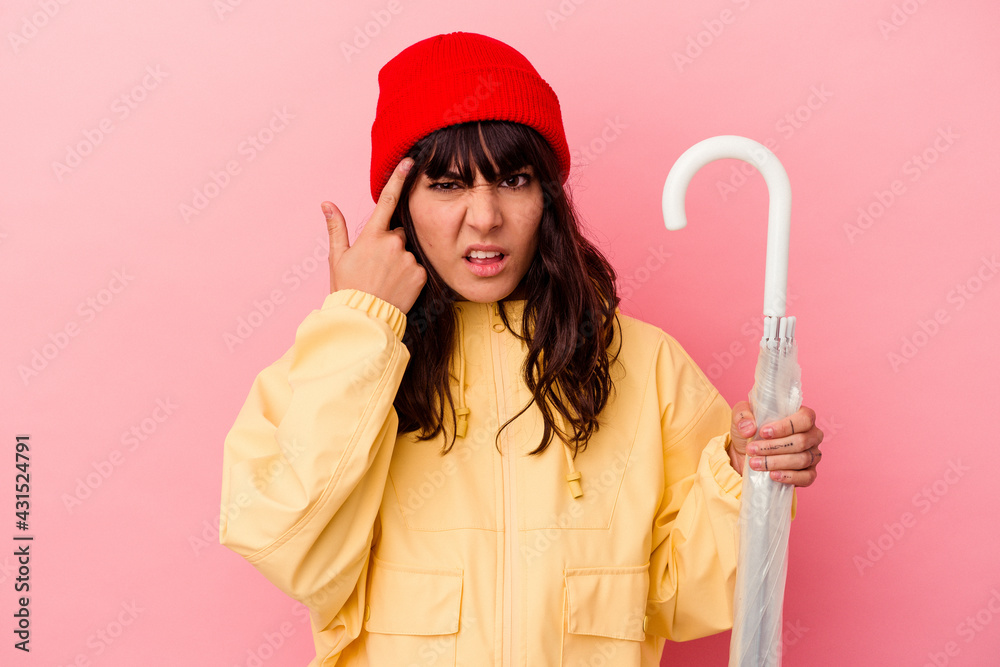 Young caucasian woman holding an umbrella isolated on pink background showing a disappointment gesture with forefinger.