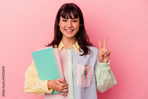 Young student caucasian woman holding books isolated on pink background showing number two with fingers.