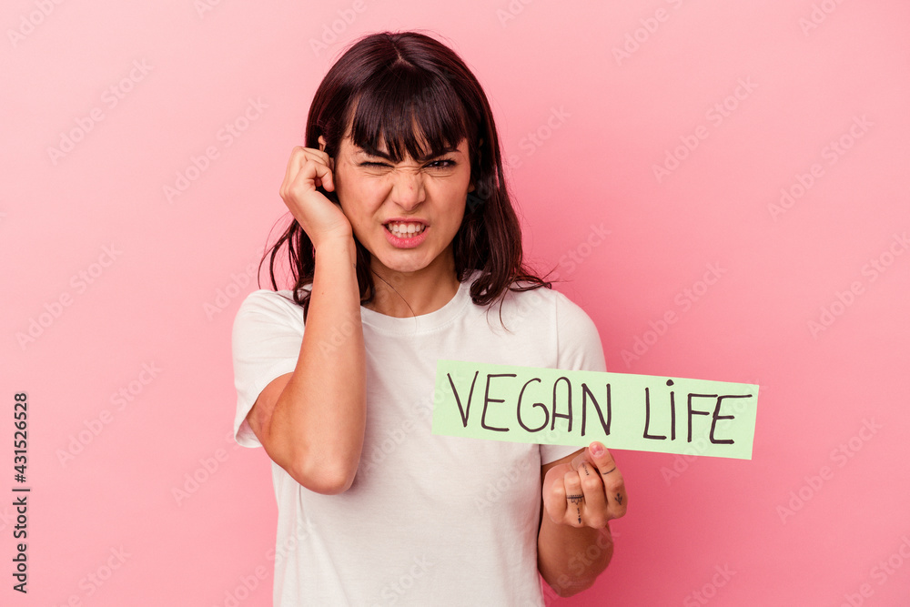 Young caucasian woman holding a vegan life placard isolated on pink background covering ears with hands. Young caucasian woman holding a vegan life placard isolated on pink background covering ears with hands.