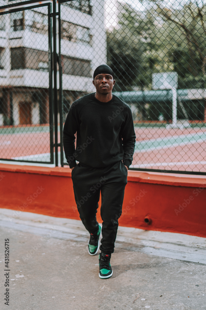 Chico negro apuesto con bandana negra en la cabeza posando frente a una cancha de baloncesto 