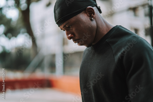 Chico negro apuesto con bandana negra en la cabeza posando frente a una cancha de baloncesto 