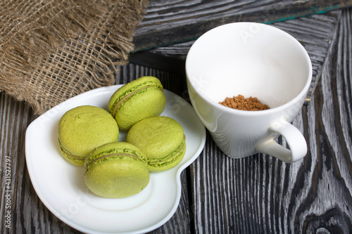 Light green macarons lie on a saucer. Next to it is a cup of coffee and a linen cloth.