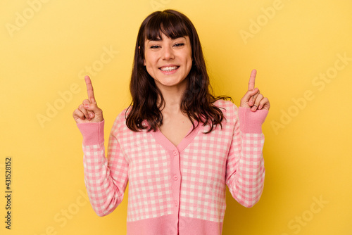 Young caucasian woman isolated on yellow background indicates with both fore fingers up showing a blank space.