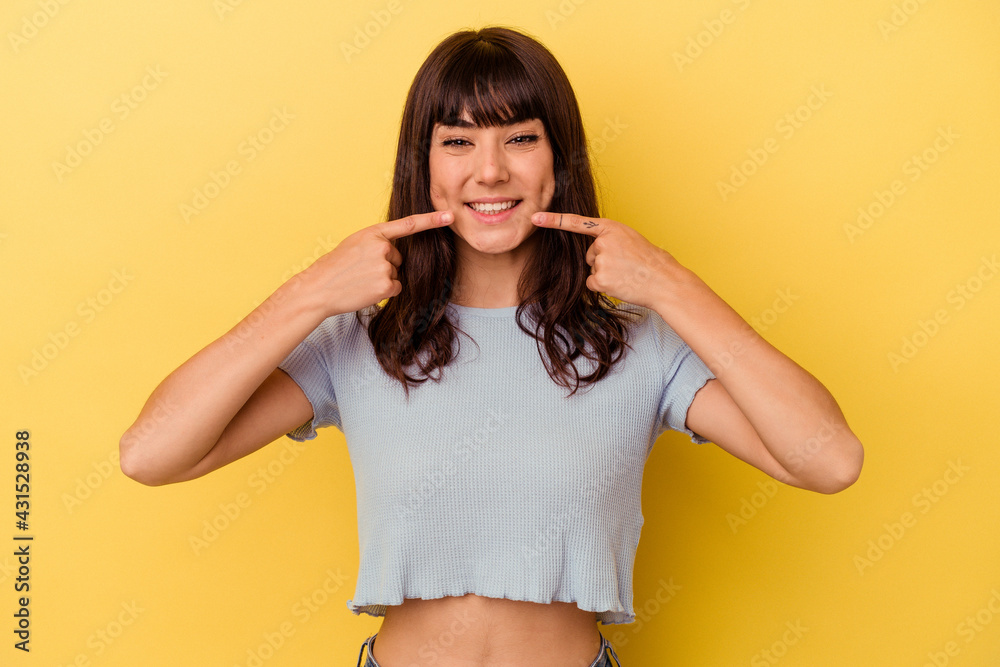 Young caucasian woman isolated on yellow background smiles, pointing fingers at mouth. Young caucasian woman isolated on yellow background smiles, pointing fingers at mouth.