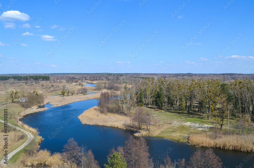 A view  from the top on the river that reflects blue sky, forest, roads, ground underneath. Beautiful landscape scenery from a drone. 