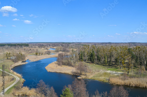 A view from the top on the river that reflects blue sky, forest, roads, ground underneath. Beautiful landscape scenery from a drone. 