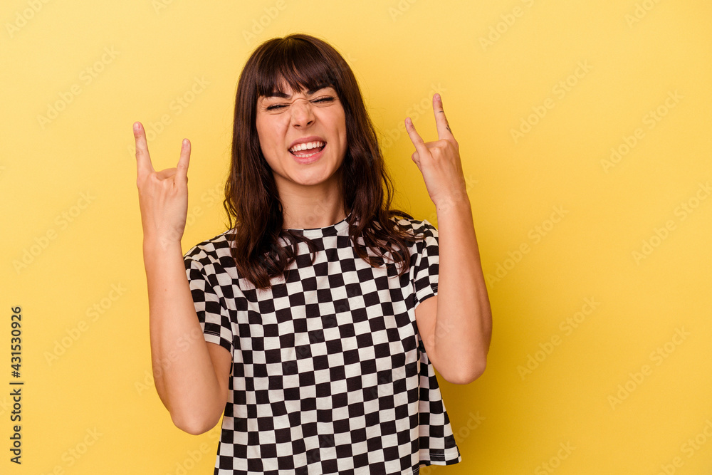 Young caucasian woman isolated on yellow background showing a horns gesture as a revolution concept.