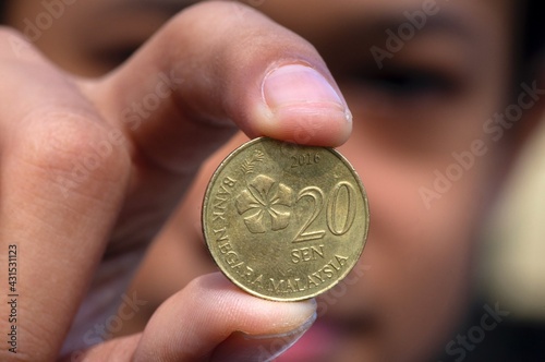 Asian child hand holding a 20 sen Ringgit Malaysia coin, selected focus and blurred background photo