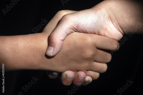 Friends and partners shaking hands with dark background. Concept of forgiving and greeting