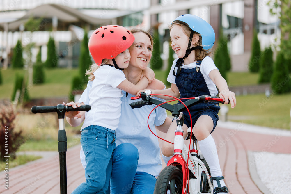 Obraz premium Mother with two cherful daughters having fun. Woman and girls in helmets riding on bicycle and scooter
