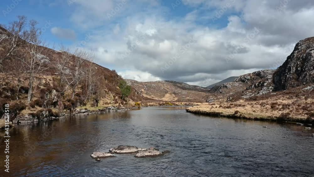 Tranquil scene of running water with audio at River Laxford, North West Highlands of Scotland. Cliffs either side of river, stones in centre, blue sky and clouds.