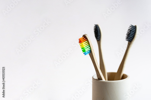 Bamboo toothbrushes in a wooden glass on a light pink background. Minimalistic still life of eco-friendly bathroom products. Zero waste  no plastic  sustainable lifestyle concept.
