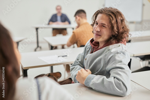 Portrait of smiling teenage boy talking to friends during lecture in school classroom, copy space