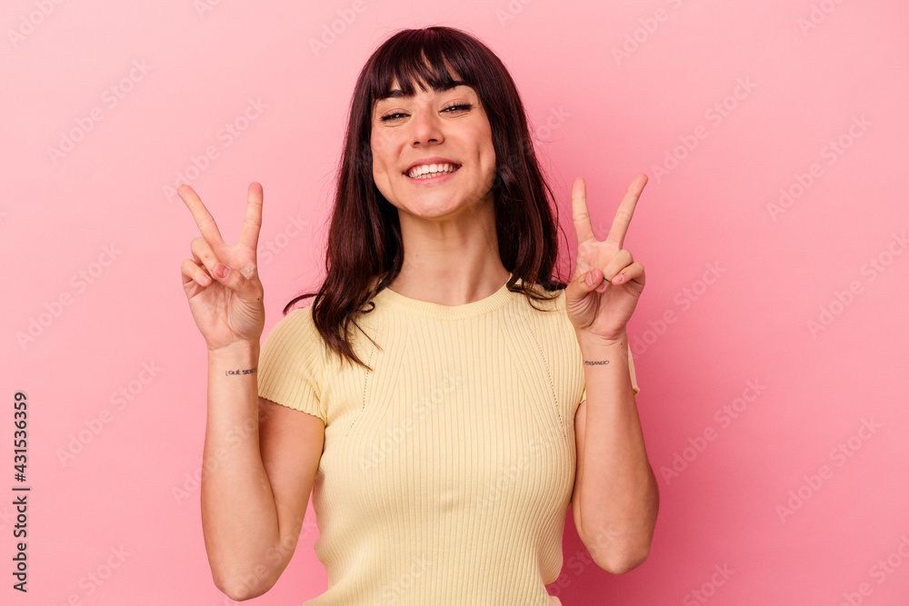 Young caucasian woman isolated on pink background showing victory sign and smiling broadly. Young caucasian woman isolated on pink background showing victory sign and smiling broadly.