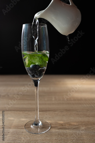 Ripe blueberries and mint in a glass of water. Splash in water on black background. 