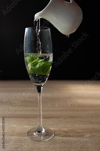 Ripe blueberries and mint in a glass of water. Splash in water on black background. 