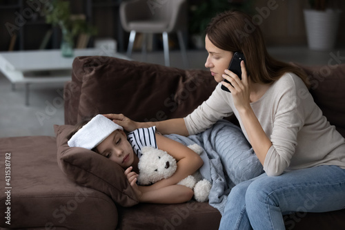 Anxious young Caucasian mom call ambulance doctor take care of sick small girl child having flu and high temperature. Worried mother contact therapist or pediatrician with little daughter feel ill.