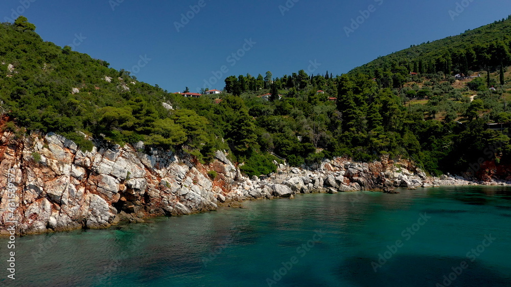 Aerial drone views over a rocky coastline, crystal clear Aegean sea waters, touristic beaches and lots of greenery in Skopelos island, Greece. A typical view of many similar Greek islands.