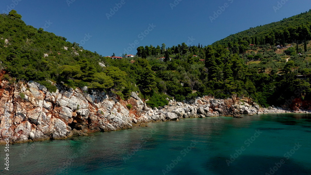 Obraz premium Aerial drone views over a rocky coastline, crystal clear Aegean sea waters, touristic beaches and lots of greenery in Skopelos island, Greece. A typical view of many similar Greek islands.