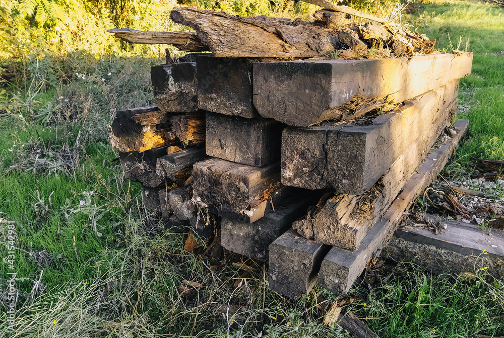 Old, used long wooden sleepers for railway repairs are scattered carelessly, lie on green grass for garbage, recycling. Preparatory work. Old, used long wooden sleepers for railway repairs are scattered carelessly, lie on green grass for garbage, recycling. Preparatory work.