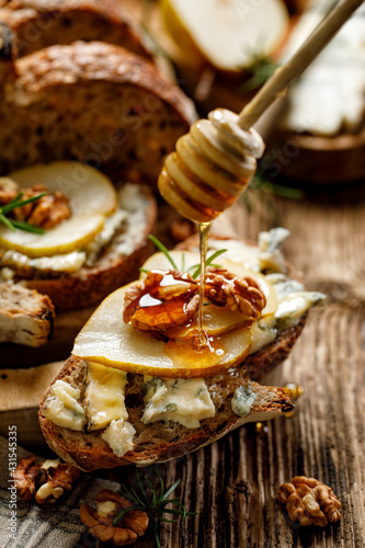 Sourdough bread sandwich with blue cheese gorgonzola, pear and walnuts, poured with honey close up view