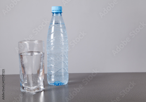Water bottle and glass, on gray background.