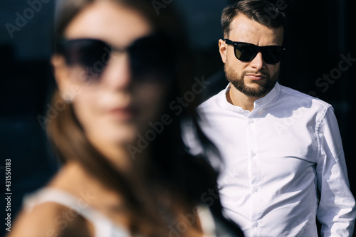 Close up fashion portrait of young couple posing on city street in summer clothes, retro sunglasses.