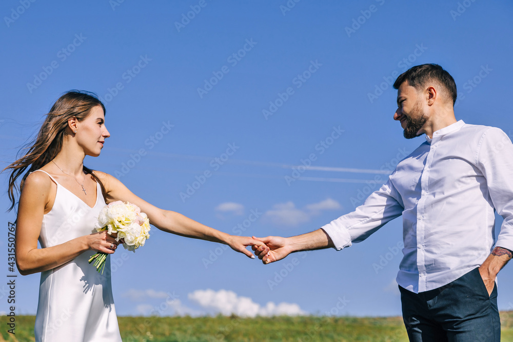 young lovers man and woman stretch hands to each other against the background of blue sky and green grass. young lovers man and woman stretch hands to each other against the background of blue sky and green grass.